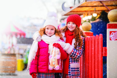 Children of red-haired sisters walk at a festively decorated Christmas market in the city.
