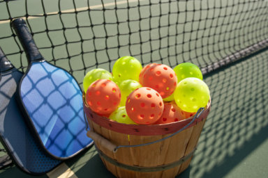 Pickleball paddles and ball in shadow of net with basket